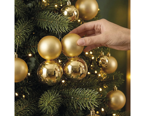 Hand dekoriert einen Christbaum mit matten und glänzenden Christbaumkugeln und einer Lichterkette.