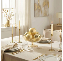 Festlich gedeckter Tisch mit beiger Tischdecke, goldenem Besteck, hohen Kerzenständer und einer Glasschale mit goldenen Weihnachtskugeln.