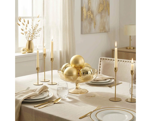 Festlich gedeckter Tisch mit beiger Tischdecke, goldenem Besteck, hohen Kerzenständer und einer Glasschale mit goldenen Weihnachtskugeln.