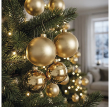 Nahaufnahme eines Christbaums mit goldenen matten und glänzenden Christbaumkugeln sowie Lichtern in einem hellen Raum.