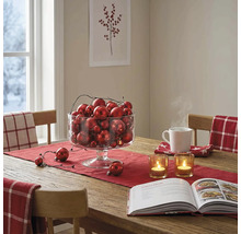 Festlich gedeckter Holztisch mit rotem Läufer, einer Glasschale voller Weihnachtskugeln, Teelichtern und einem Kochbuch.