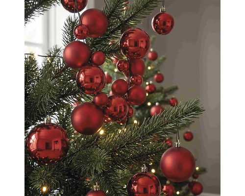 Rote Christbaumkugeln in verschiedenen Größen mit matter und glänzender Oberfläche an einem Christbaum.