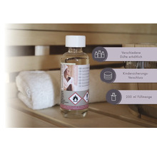 Saunaduft Kokos-Vanille in einer 250 Milliliter Flasche mit Kindersicherungs-Verschluss in einer Sauna neben einem Handtuch und einem Holzkübel.
