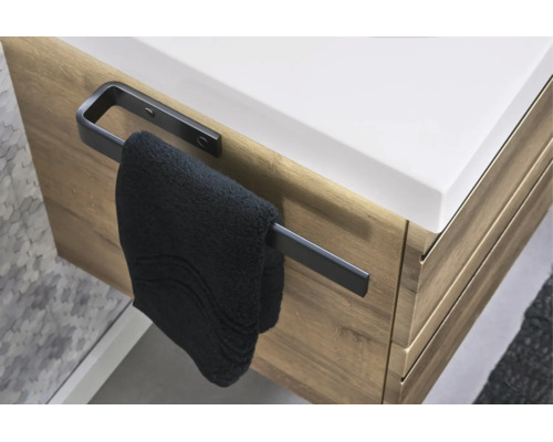 Schwarzer Handtuchhalter seitlich an einem Waschtischunterschrank in Holzoptik montiert mit einem Handtuch.