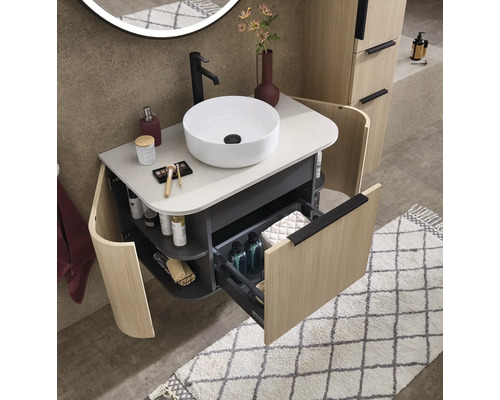 Moderner, gut organisierter Waschtisch mit rundem Aufsatzbecken, geöffneter Schublade, geschwungenen Seitenregalen und Fronten in Holzoptik.