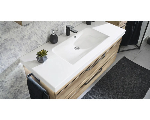 Moderner Badezimmer-Waschtisch mit weißem Waschbecken, Holzunterschrank und schwarzer Armatur vor einer Wand mit Sechseck-Fliesen.