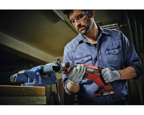 Ein Handwerker nutzt eine Einhell Akku-Säbelsäge, um ein Kunststoffrohr in einem Schraubstock zu schneiden.