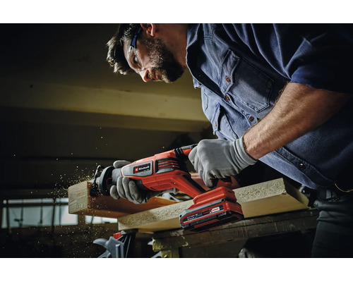 Handwerker mit Schutzbrille nutzt eine Einhell Akku Reciprosäge zum Schneiden eines Holzbretts in der Werkstatt.