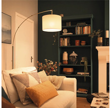 Moderne Bogenlampe mit Stoffschirm neben einem hellen Sofa in einem gemütlich eingerichteten Wohnzimmer mit dunklem Bücherregal.