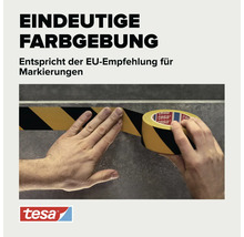 Eine Person klebt schwarz gelbes Warnband auf einen Boden. Das tesa Markierungsband entspricht der europäischen Empfehlung für Kennzeichnungen.