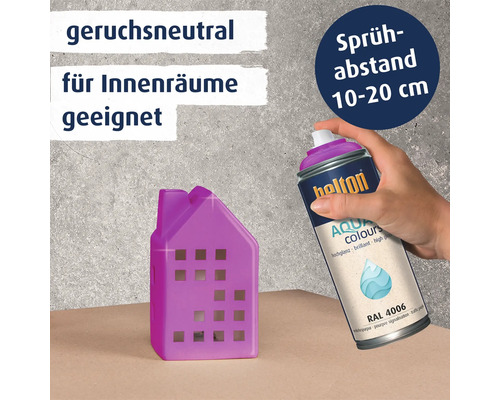 Eine Hand sprüht mit einer Spraydose Belton Aqua Colours in Verkehrs-purpur RAL 4006 ein kleines Deko Haus an für den Innenbereich.