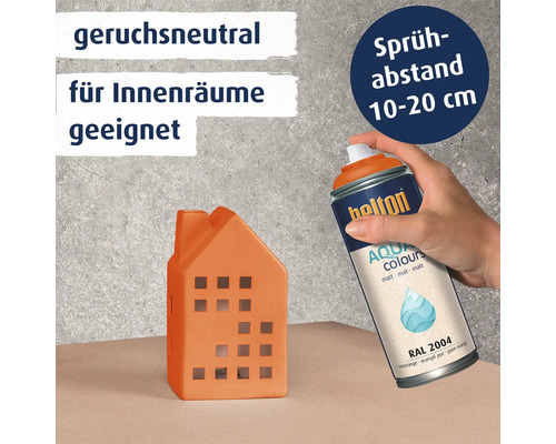 Eine Hand sprüht mit der Helton Aqua Colours Sprühdose auf ein kleines Hausobjekt mit dem Hinweis auf Geruchsneutralität und Sprühabstand.
