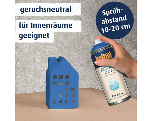 Eine Hand hält eine Belton Aqua Sprühdose und lackiert ein kleines Hausmodell in Enzianblau.