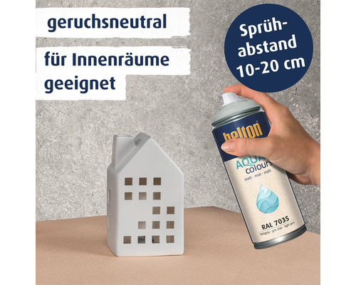 Eine Hand hält eine Sprühdose Belton Aqua Colours matt RAL 7035 zum Bemalen eines kleinen Keramikhauses mit Hinweisen zu Geruchsneutralität