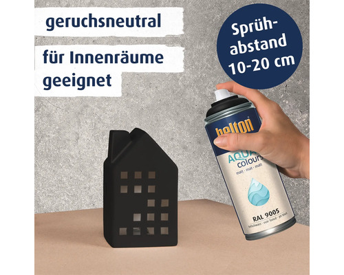 Hand hält eine Sprühdose mit Aqua Colours Lackspray in der Farbe Tiefschwarz zum Besprühen einer kleinen Hausfigur aus Keramik