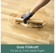 Hand in Arbeitshandschuh verfugt Parkettboden mit Fugenspachtel aus Holz und Metall