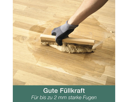 Hand in Arbeitshandschuh verfugt Parkettboden mit Fugenspachtel aus Holz und Metall