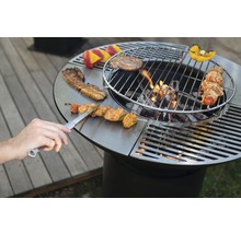 Runder Grill mit Speisen und Grillwerkzeug auf der Grillfläche