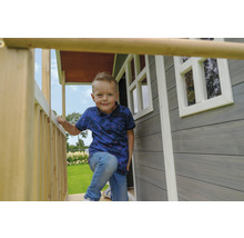 Ein Junge steht auf der Veranda eines Holzspielhauses mit Fenstern.