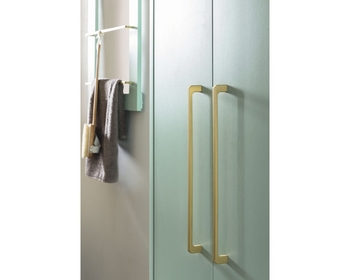 Detailansicht eines Badezimmers mit einem Schrank mit zwei goldenen Griffen und einem Regal mit Handtuch und Bürste.