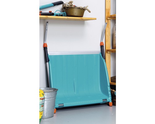 Eine blaue Schneeschaufel steht in einem Lagerraum an der Wand.