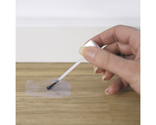 Eine Hand verwendet einen Pinsel zur Ausbesserung eines Holzboden.