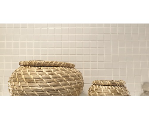 Zwei geflochtene Körbe mit Deckel vor einer Wand mit kleinen quadratischen Fliesen.
