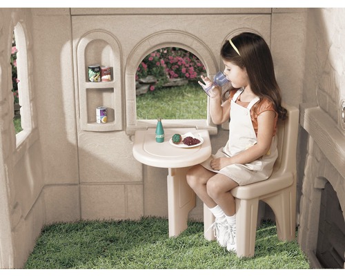 Mädchen trinkt in einem Spielhaus am Tisch