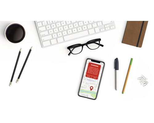 Tastatur, Brille, Smartphone mit Warnmeldung, Notizbuch und Stifte auf einem Schreibtisch
