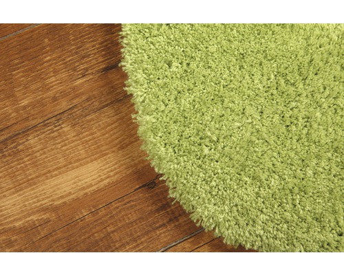 Detailansicht eines grünen Teppichs mit Shaggy Flor auf einem Holzboden