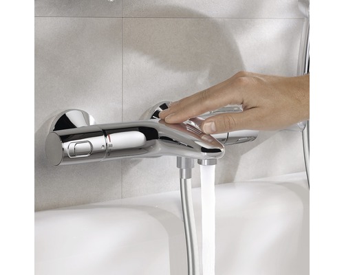 Aufnahme einer Hand, die einen verchromten Duschmischer betätigt, aus dem Wasser fließt.