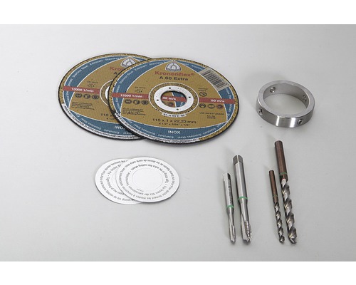 Zwei Trennscheiben, ein Metallring, zwei Gewindebohrer, zwei Bohrer und mehrere runde Aufkleber liegen auf einem Tisch.