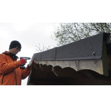 Mann befestigt Dachpappe mit einem Akku-Schrauber auf einem Holzschuppen.