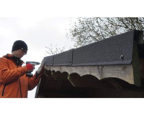 Mann befestigt Dachpappe mit einem Akku-Schrauber auf einem Holzschuppen.