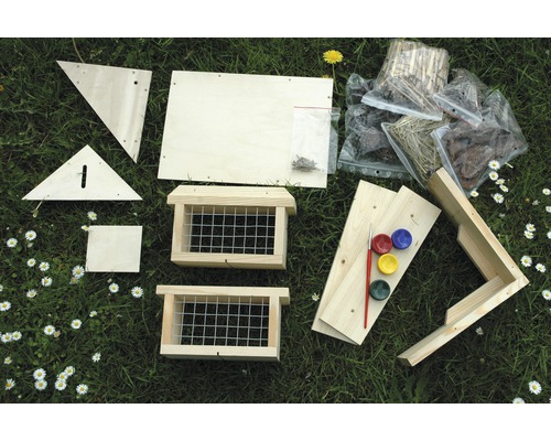Bausatz für ein Futterhaus mit Farben, Pinsel, Schrauben und Naturmaterialien auf einer Wiese