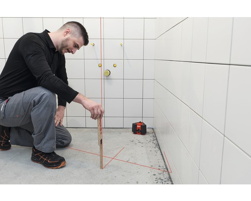 Handwerker mit Laser-Wasserwaage und Zollstock im Badezimmer bei der Arbeit