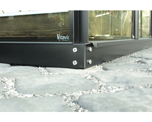 Detailansicht eines Gewächshausfundaments aus Metall mit Schrauben auf Steinboden