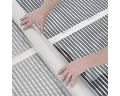 Person rollt eine elektrische Fußbodenheizung aus.