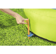 Eine Person befestigt mit einem Hering eine grüne Hüpfburg im Gras.