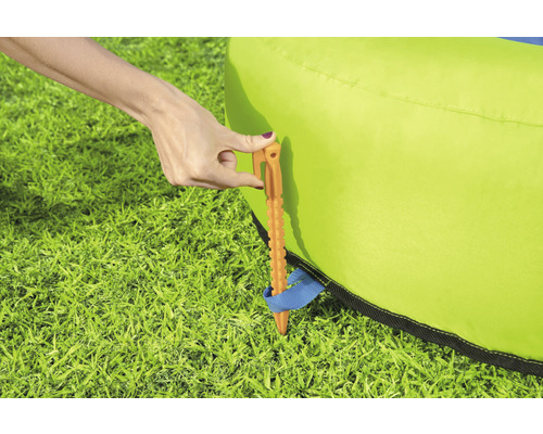 Eine Person befestigt mit einem Hering eine grüne Hüpfburg im Gras.