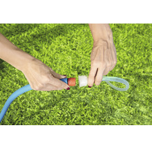 Gartenarbeitsszene mit zwei Händen, die einen Gartenschlauch verbinden, im Hintergrund Rasen