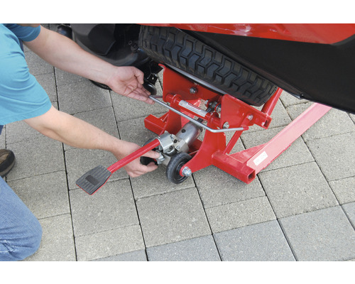 Eine Person bedient einen roten Rasentraktorheber unter einem Rasentraktor.