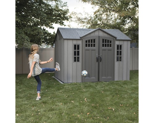 Gartenschuppen im Garten mit einem Mädchen, das einen Fußball tritt