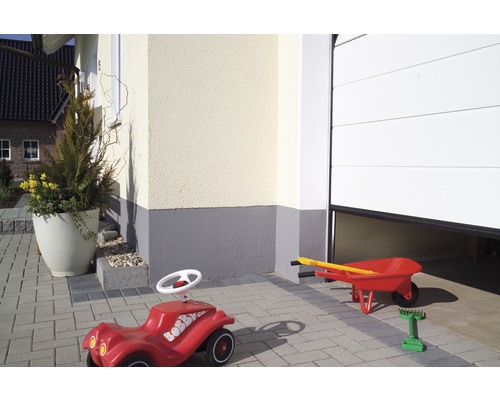 Außenansicht eines Hauses mit einem Bobby Car und einer Schubkarre vor einer Garage