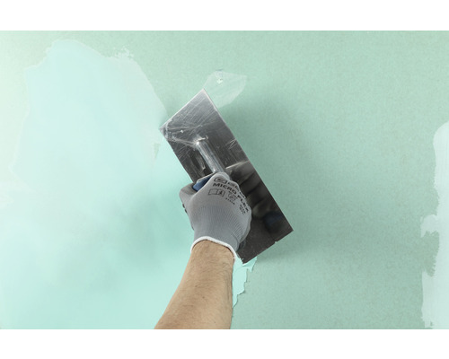 Handwerker mit einer Spachtel beim Auftragen von Spachtelmasse auf eine Wand