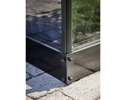 Detailaufnahme einer Glaskonstruktion mit Metallrahmen und Schrauben auf Pflastersteinen.