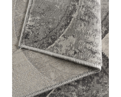 Detailansicht eines grauen Teppichs mit abstraktem Muster und gekettelten Kanten.