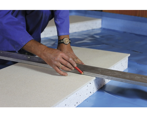 Handwerker zeichnet mit Bleistift und Richtscheit auf einer Bauplatte.