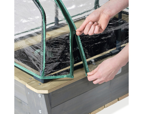 Detailaufnahme eines Hochbeetes mit durchsichtiger Abdeckung und Reißverschluss, der von Händen geöffnet wird.