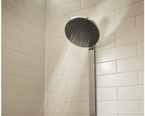 Aufputz-Duschkopf mit Wasserstrahl in einem Badezimmer mit hellen Fliesen.